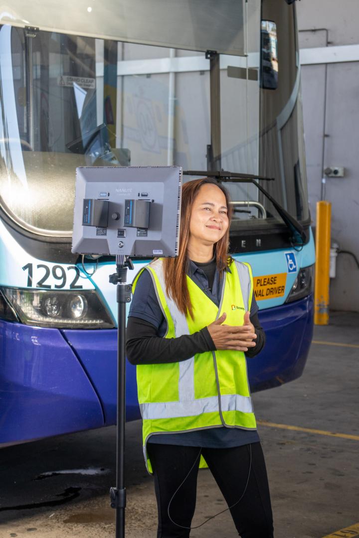 Bus driver standing in front of a blue bus being filmed